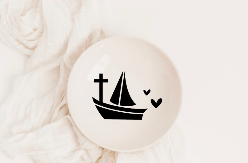 May include: A white ceramic dish with a black silhouette of a sailboat with a cross on the bow and three hearts.