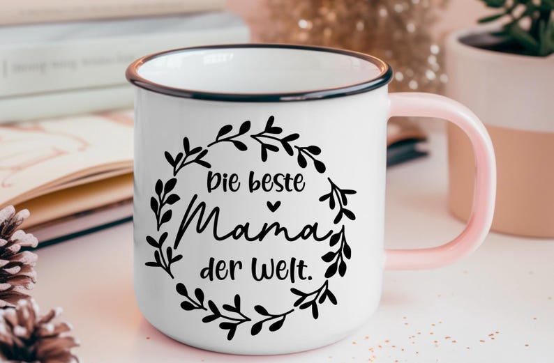 May include: White enamel mug with a black rim and pink handle. The mug has a black floral design with the text "Die beste Mama der Welt."