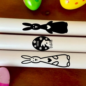 May include: Three white candles with black bunny and Easter egg designs. The candles are decorated with the text "Frohe Ostern" which means "Happy Easter" in German.