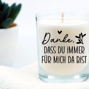 May include: A white candle in a clear glass jar with a black inscription that reads "Danke. Dass du immer f&uuml;r mich da bist".