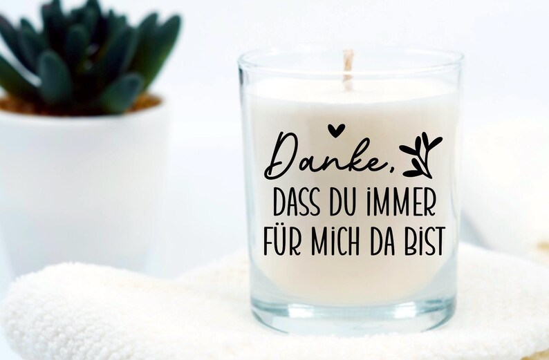 May include: A white candle in a clear glass jar with a black inscription that reads "Danke. Dass du immer f&uuml;r mich da bist".