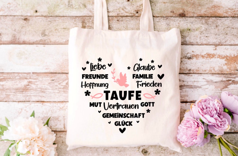 May include: White canvas tote bag with black text that reads "*Liebe* FREUNDE Hoffnung *Glaube* FAMILIE Frieden *TAUFE* MUT Vertrauen GOTT GEMEINSCHAFT *GL&Uuml;CK*" with a pink dove and fish graphic.