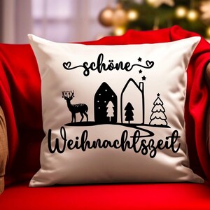 May include: White throw pillow with black text and illustrations. The text reads "sch&ouml;ne Weihnachtszeit" which translates to "beautiful Christmas time". The illustrations include a deer, two houses, and two Christmas trees.