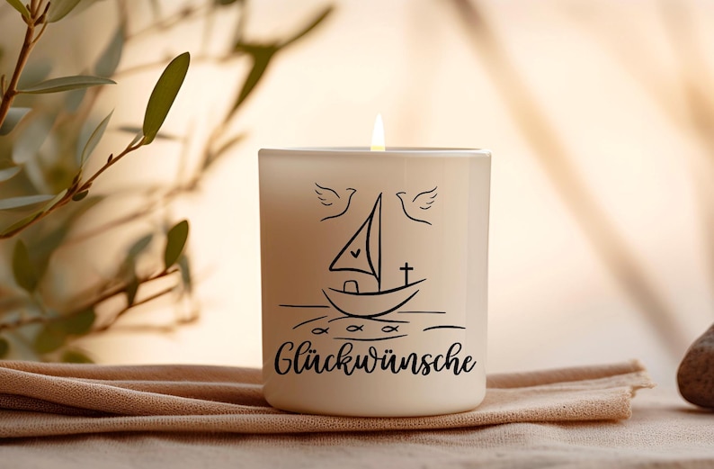 May include: A lit, off-white candle in a glass container. The candle has a black line drawing of a sailboat, doves, and the word "Gl&uuml;ckw&uuml;nsche". The candle sits on a tan cloth.