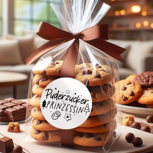 May include: A clear plastic bag filled with chocolate chip cookies tied with a brown ribbon. A white sticker with black text reads "Puderzucker Prinzessin" with a small tree and star design.