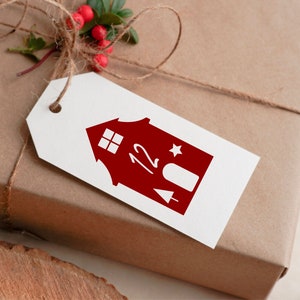 K&ouml;nnte beinhalten: Ein wei&szlig;es Geschenkanh&auml;nger mit einer roten Haus-Illustration. Das Haus hat ein Fenster, einen Stern und die Nummer 12 darauf.