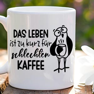 May include: White ceramic coffee mug featuring a black cartoon bird holding a coffee cup. The mug has the German text "DAS LEBEN ist zu kurz f&uuml;r schlechten KAFFEE", which translates to "Life is too short for bad coffee."