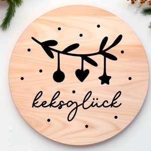 May include: A round wooden sign with a black and white illustration of a branch with ornaments and the text "keksgl&uuml;ck".
