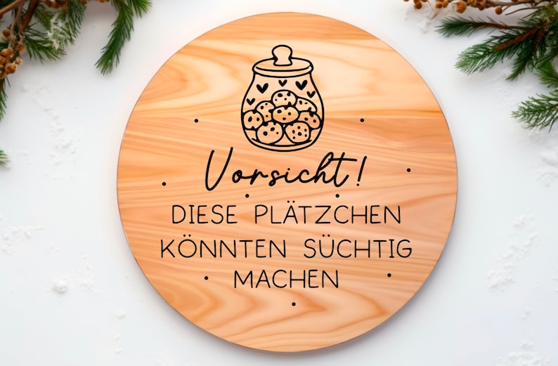 May include: A round wooden sign with a black and white illustration of a cookie jar filled with cookies. The sign reads "Vorsicht! Diese Pl&auml;tzchen k&ouml;nnten s&uuml;chtig machen."