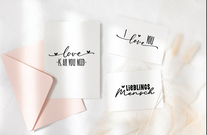 Puede incluir: Tres tarjetas blancas con caligraf&iacute;a negra. Las tarjetas dicen "love is all you need", "I love you" y "Lieblings Mensch".