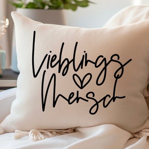 May include: A white throw pillow with black text that reads "Lieblings Mensch" with a small heart symbol.