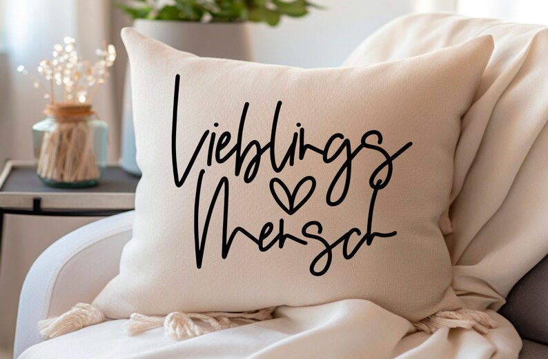 May include: A white throw pillow with black text that reads "Lieblings Mensch" with a small heart symbol.
