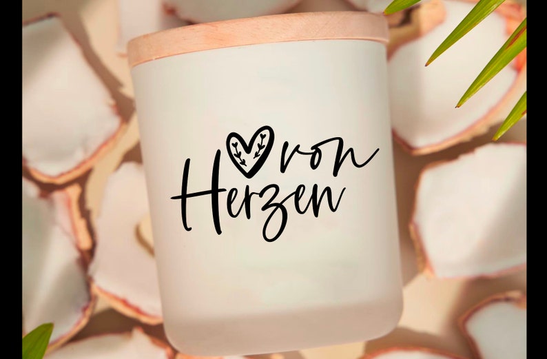 May include: White candle with a wooden lid and a black heart with leaves design. The text "von Herzen" is written in black script on the candle.