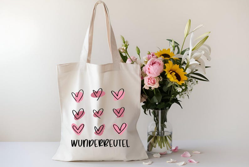 May include: White canvas tote bag with pink and black hearts and the text "WUNDERBEUTEL". The bag is next to a vase of flowers.