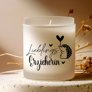 K&ouml;nnte beinhalten: Wei&szlig;e, gefrostete Glaskerze mit einem schwarzen Igel-Motiv und dem Text "Lieblings Erzieherin" in schwarzer Schrift.