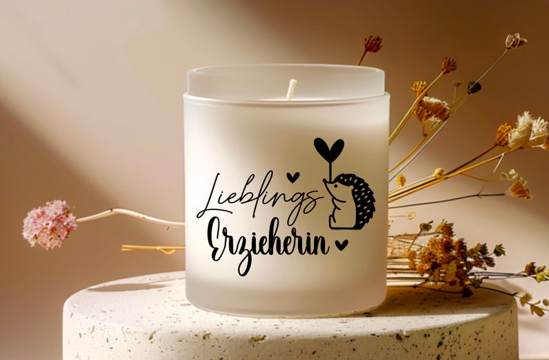 K&ouml;nnte beinhalten: Wei&szlig;e, gefrostete Glaskerze mit einem schwarzen Igel-Motiv und dem Text "Lieblings Erzieherin" in schwarzer Schrift.