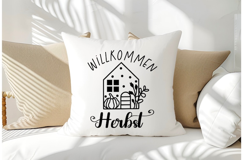 May include: White throw pillow with black text that says "Willkommen Herbst" and a black and white illustration of a house with a pumpkin and fall foliage.