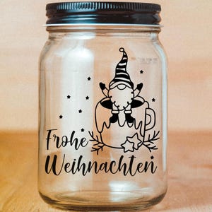 May include: A clear glass jar with a black lid and a black and white design of a gnome sitting in a mug with the text "Frohe Weihnachten" on the front.
