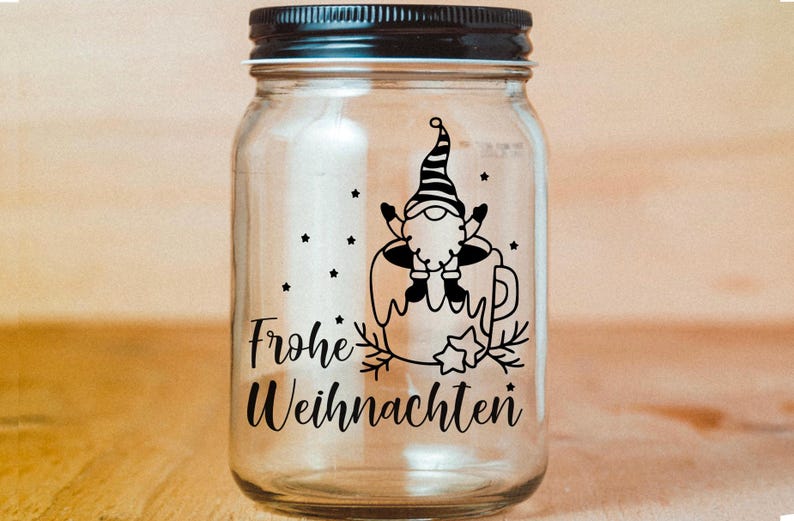 May include: A clear glass jar with a black lid and a black and white design of a gnome sitting in a mug with the text "Frohe Weihnachten" on the front.