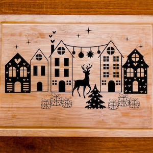 Puede incluir: Una tabla de cortar de madera con un dise&ntilde;o de pueblo navide&ntilde;o. El dise&ntilde;o presenta cinco casas, un reno, un &aacute;rbol de Navidad y regalos. Las casas son blancas y negras con detalles de coraz&oacute;n y estrella. El reno es negro y el &aacute;rbol de Navidad es verde.