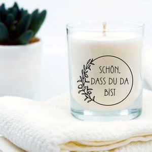 Op de afbeelding: Een witte kaars in een glazen pot met een zwart-wit label waarop "SCH&Ouml;N, DASS DU DA BIST" staat. De kaars staat op een witte handdoek.