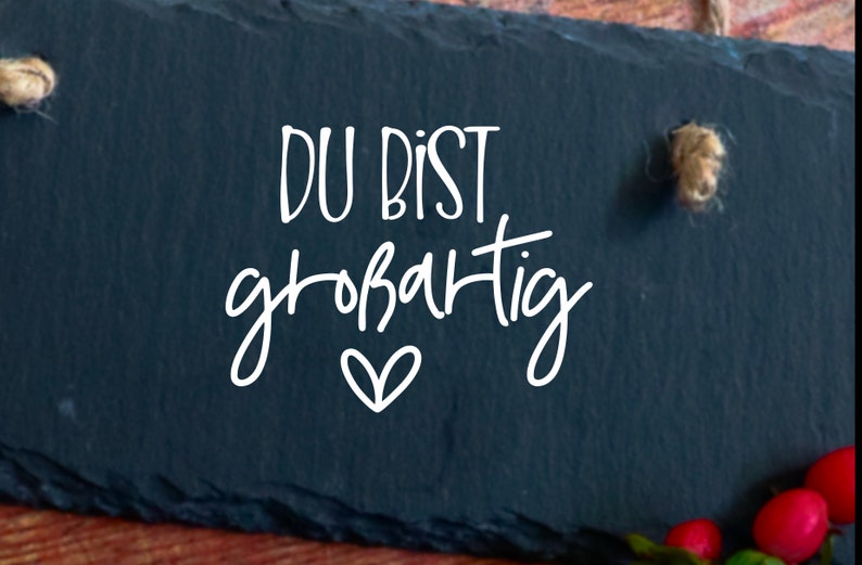 May include: A black slate sign with white text that reads "DU BIST gro&szlig;artig" with a small heart underneath.