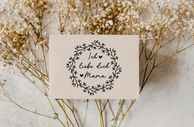 May include: A white card with a black floral wreath and the text "Ich liebe dich Mama" with small hearts.