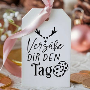 May include: White gift tag with black text and a reindeer illustration. The text reads "Vers&uuml;&szlig;e dir den Tag" which translates to "Sweeten your day".