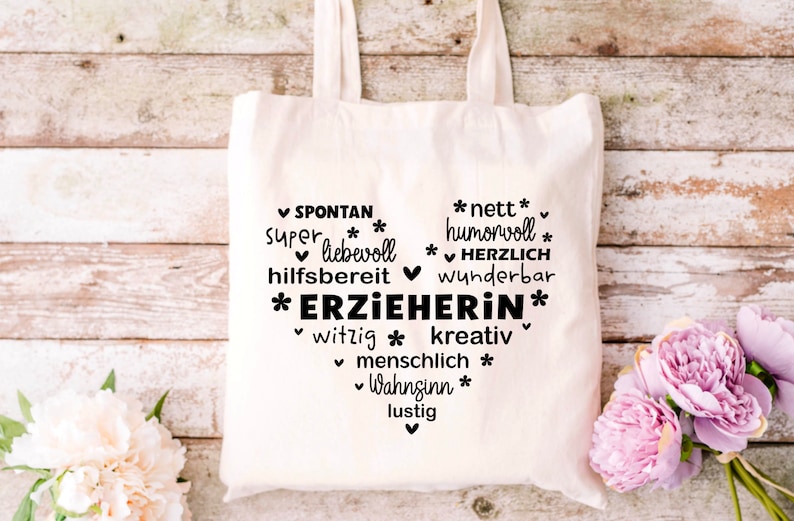 K&ouml;nnte beinhalten: Eine wei&szlig;e Stofftasche mit schwarzem Text, der "SPONTAN, super liebevoll, hilfsbereit, *ERZIEHERIN*, witzig, kreativ, menschlich, Wahnsinn, lustig" und "*nett*, humorvoll, *HERZLICH, wunderbar" lautet.