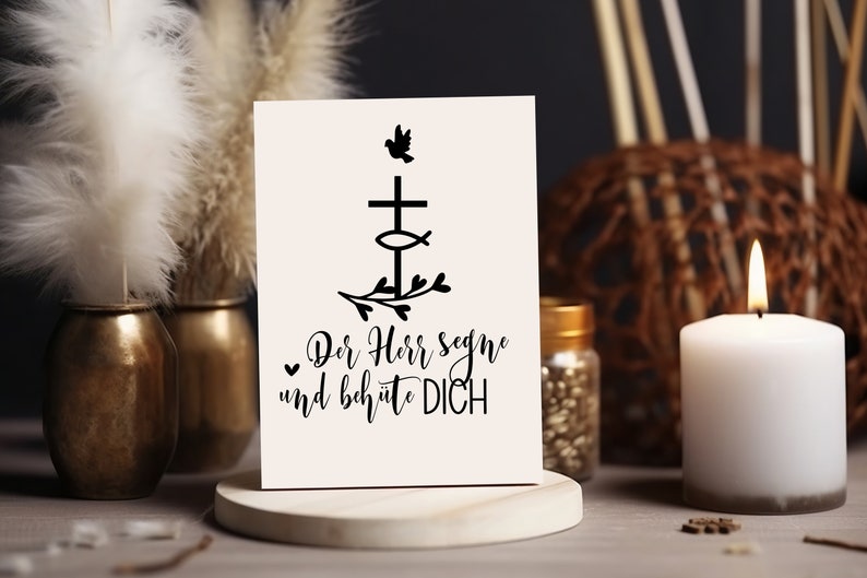 Peut inclure: Une carte blanche avec du texte noir et un graphique noir d'une croix avec un poisson et une colombe au-dessus. Le texte dit "Der Herr segne und beh&uuml;te DICH". La carte est pos&eacute;e sur un support en bois.
