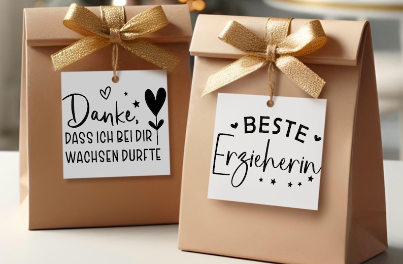 May include: Two beige gift bags with gold ribbon bows. Each bag has a white tag with black script. One says "Danke, DASS ICH BEI DIR WACHSEN DURFT" and the other says "BESTE Erzieherin".