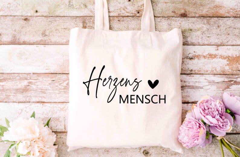 May include: White canvas tote bag with black text that reads "Herzens Mensch" with a small black heart symbol.