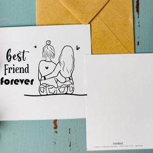 May include: A white card with black text that reads "best friend forever". The card features a line drawing of two women sitting back to back with their arms around each other.