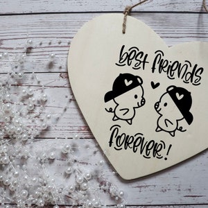 Puede incluir: Un letrero de madera blanco en forma de coraz&oacute;n con el texto "Best Friends Forever!" en escritura negra. Dos cerdos de dibujos animados con sombreros se miran con corazones sobre sus cabezas.