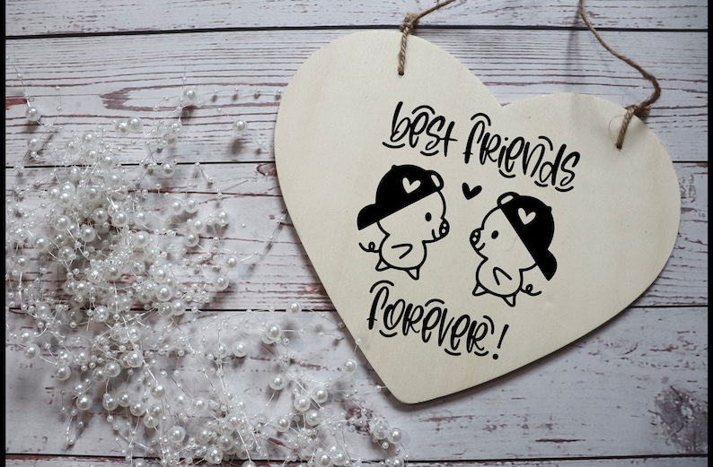 Puede incluir: Un letrero de madera blanco en forma de coraz&oacute;n con el texto "Best Friends Forever!" en escritura negra. Dos cerdos de dibujos animados con sombreros se miran con corazones sobre sus cabezas.
