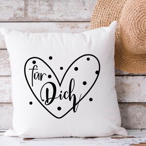 Puede incluir: Almohada blanca con un dise&ntilde;o de coraz&oacute;n negro que dice "f&uuml;r Dich" con puntos negros alrededor del coraz&oacute;n.