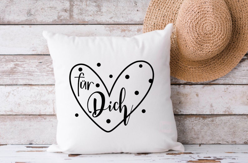 Puede incluir: Almohada blanca con un dise&ntilde;o de coraz&oacute;n negro que dice "f&uuml;r Dich" con puntos negros alrededor del coraz&oacute;n.