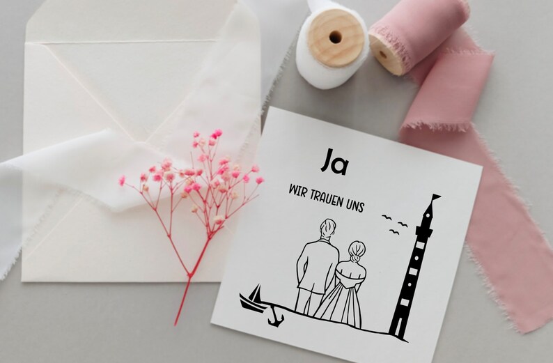 May include: A white card with black text and a black line drawing of a couple standing in front of a lighthouse. The text on the card reads "Ja Wir Trauen Uns".