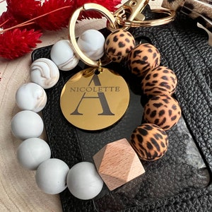 May include: A gold keychain with a round charm that says "NICOLETTE A" surrounded by white and leopard print beads.