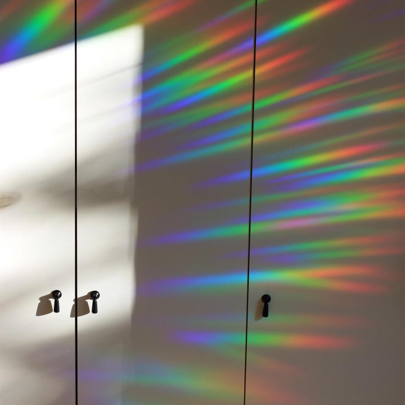 Pu&ograve; includere: Due ante di armadio bianche con pomelli neri. Le ante sono ricoperte da un film a prisma arcobaleno che crea un motivo colorato e iridescente.