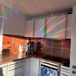 Pu&ograve; includere: Una cucina con armadi bianchi e una stufa in acciaio inox. Gli armadi hanno un film a prisma arcobaleno, creando uno spettacolo di luci colorate. C'&egrave; una macchina per il caff&egrave; e un macinacaff&egrave; sul bancone.