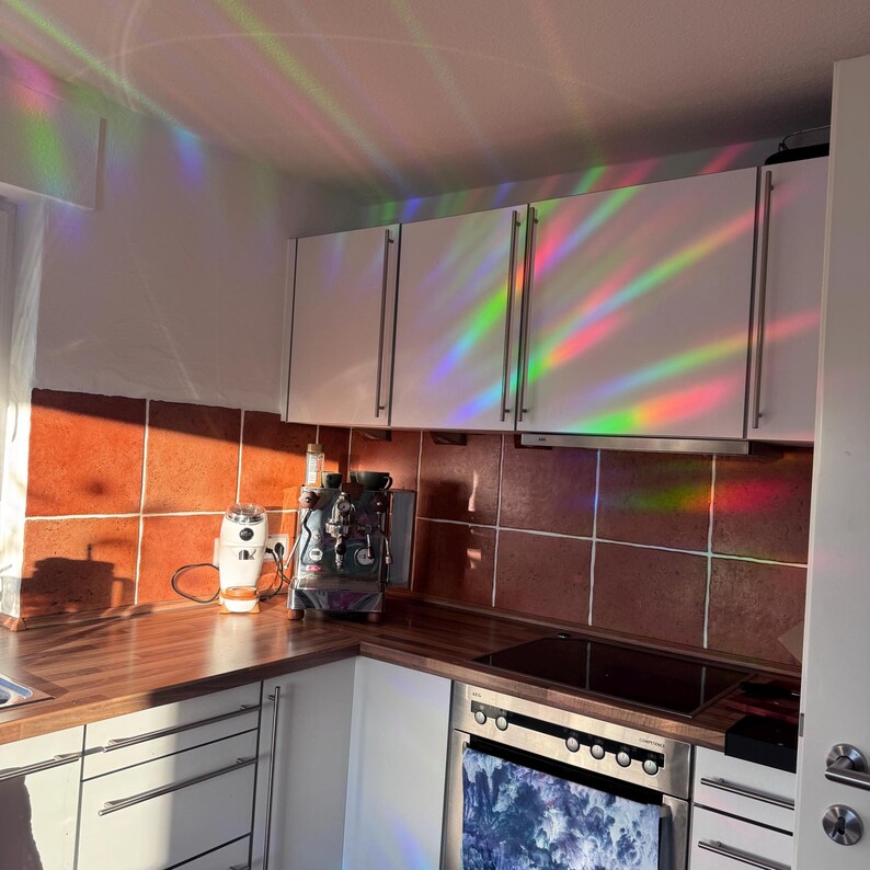 Pu&ograve; includere: Una cucina con armadi bianchi e una stufa in acciaio inox. Gli armadi hanno un film a prisma arcobaleno, creando uno spettacolo di luci colorate. C'&egrave; una macchina per il caff&egrave; e un macinacaff&egrave; sul bancone.