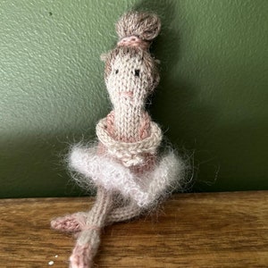 Könnte beinhalten: Eine gestrickte Puppe, die ein rosa-weißes Tutu trägt. Die Puppe hat braunes Haar und ein gestricktes Gesicht.