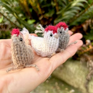 May include: Three knitted bird figurines, one white with a red comb, one grey with a red comb, and one brown with a red comb.