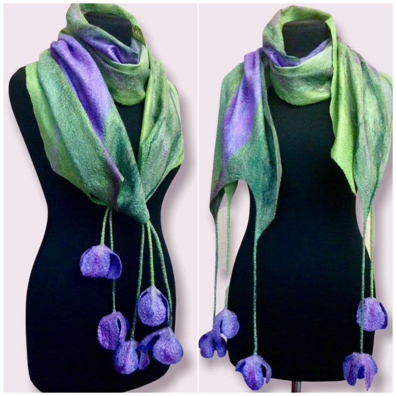 May include: A green and purple felted wool scarf with purple flower accents. The scarf is draped over a black mannequin.