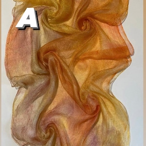 Può includere: Un tessuto leggero e trasparente in tonalità di arancione, giallo e marrone. Il tessuto è drappeggiato e piegato, creando un design testurizzato e astratto. Il testo "Silk rarefied" è stampato nella parte inferiore dell'immagine.