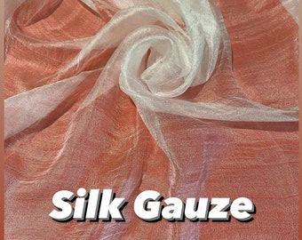 Pode incluir: Tecido de gaze de seda branca com textura suave e transparente. O tecido é drapeado e dobrado, criando um visual delicado e fluido. O texto "Silk Gauze" é impresso em letras brancas em negrito no tecido.