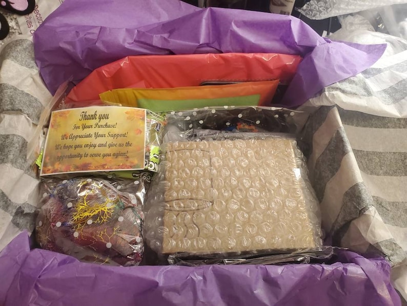 May include: A purple and white gift box filled with items wrapped in bubble wrap and tissue paper. A thank you note reads "Thank you for your purchase! We appreciate your support! We hope you enjoy and give us the opportunity to serve you again."