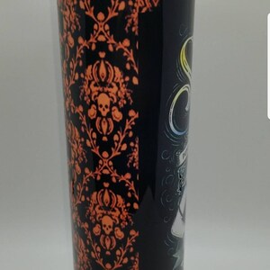May include: A black and orange stainless steel tumbler with a spooky Halloween design. The design features a skull and crossbones, a ghost, and the words "Haunted Mansion".