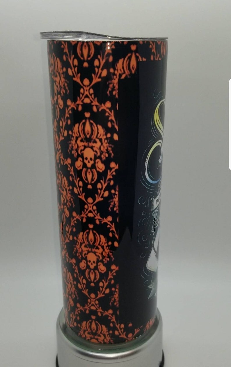 May include: A black and orange stainless steel tumbler with a spooky Halloween design. The design features a skull and crossbones, a ghost, and the words "Haunted Mansion".